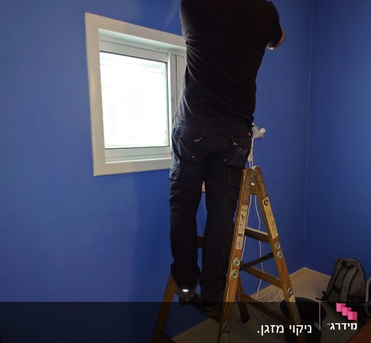 אדם מתקין מזגן על קיר כחול בעזרת סולם